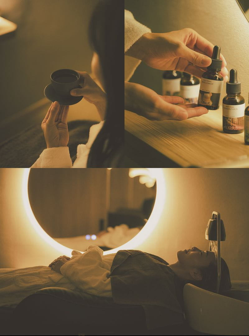 Tea, aroma oils and a guest resting at a head spa basin beneath a softly glowing mirror