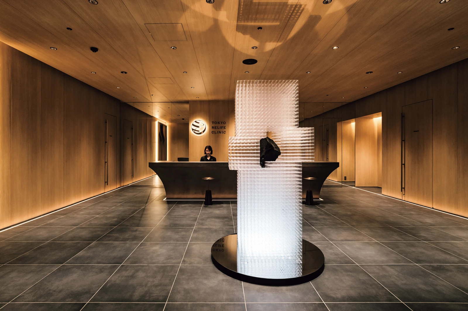 The reception of Tokyo ReLife Clinic, with warm timber, stone and an illuminated central installation